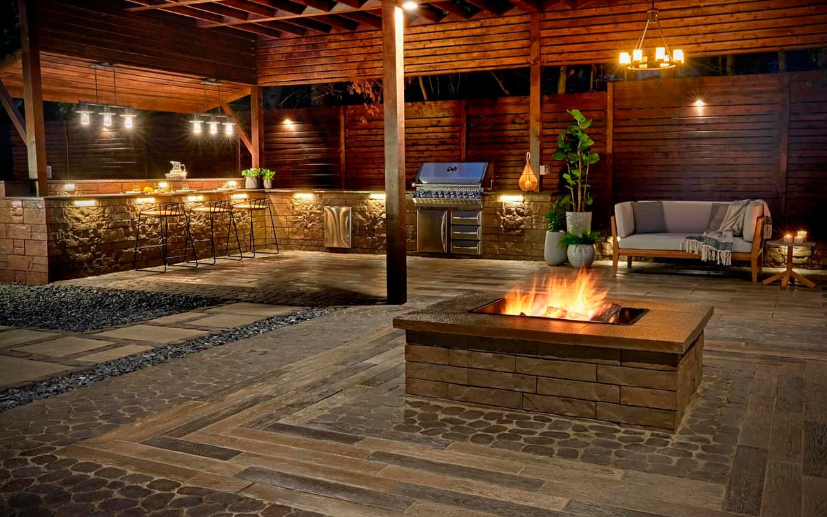 Covered patio with built-in fire pit, outdoor kitchen, and warm lighting designed by Expert Hardscaping in Fort Worth, TX
