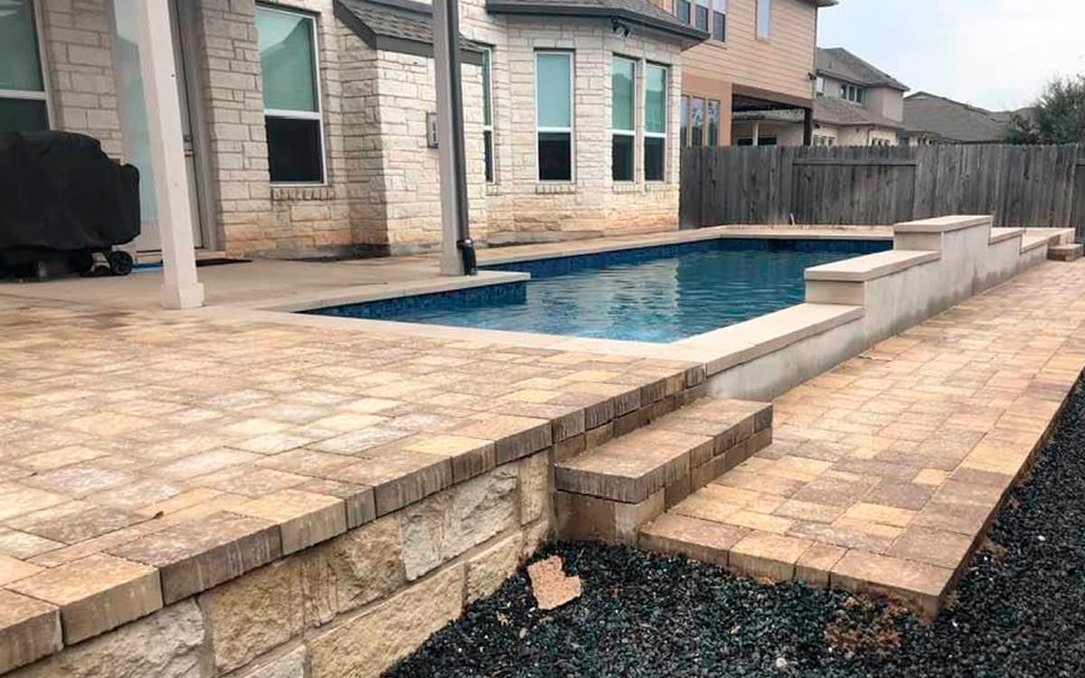 Backyard pool with stone paver deck and raised wall built by Expert Hardscaping in Fort Worth, TX